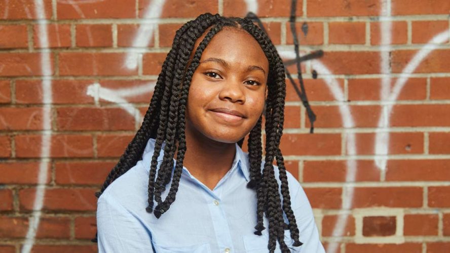 Young female Black mentee smiling in front of a brick wall