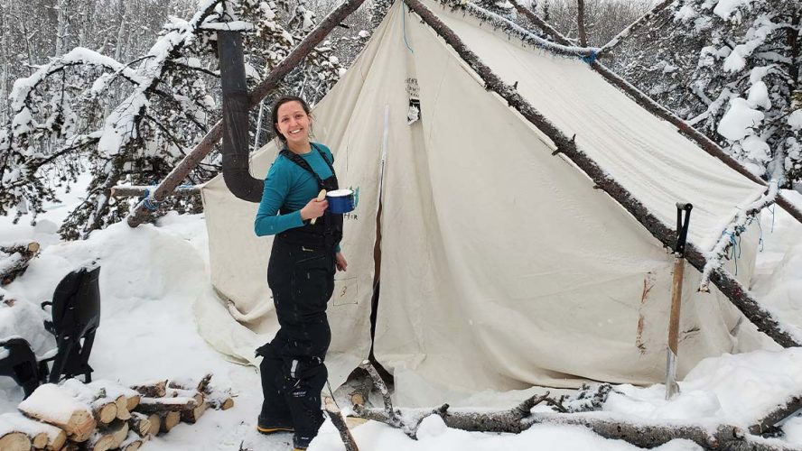 Aurora College student standing outside a tent in a snow and grinning