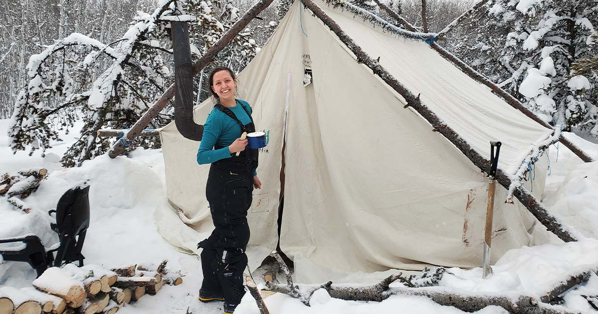 Aurora College student standing outside a tent in a snow and grinning