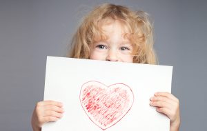 dziecko trzymające w dłoniach kartę z narysowanym sercem