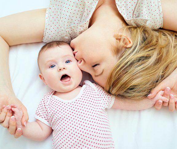 młoda mama całująca swoje niemowlę na łóżku