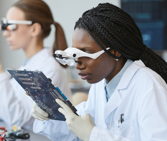 young woman wearing magnifying glasses and inspecting electronic parts in quality control lab