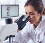 Shot of a cheerful young female scientist looking through the lens of a microscope while being seated inside of a laboratory