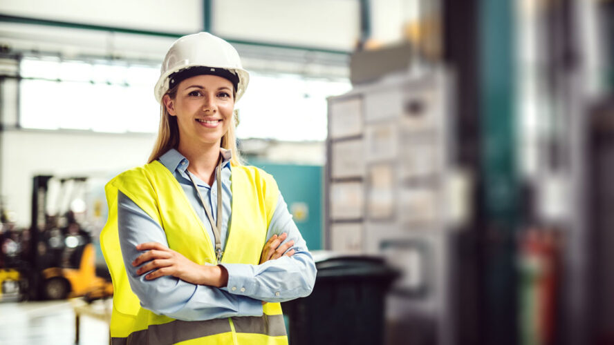 A portrait of an industrial woman engineer standing in a factory, arms crossed