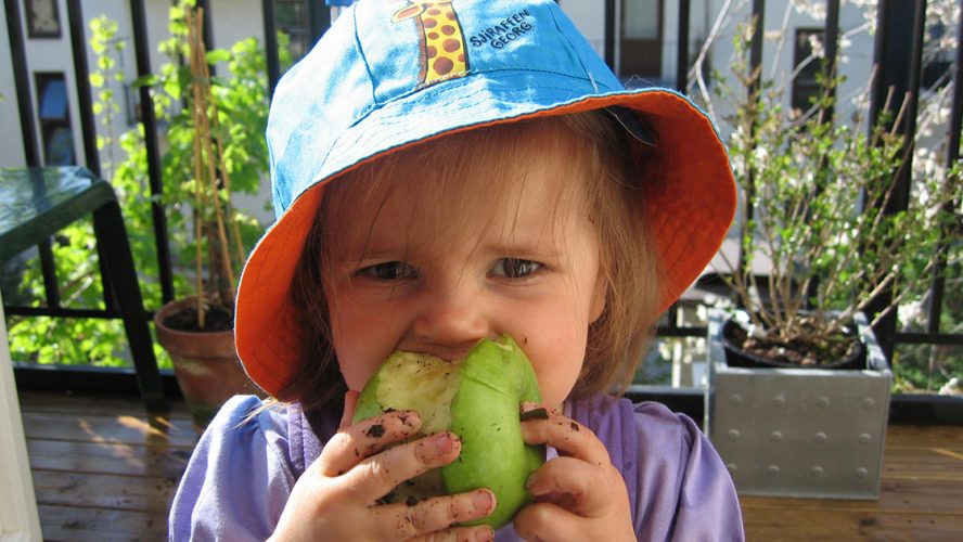 Liten jente med solhatt og eple i munnen