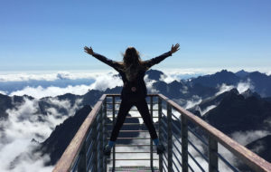 kvinne med ryggen til som står på en bro med fjell utsikt