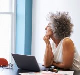 Moden kvinde sidder foran computer og stirre ud ad vinduet