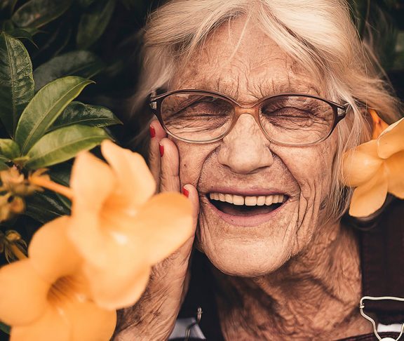 Grinende ældre kvinde ved blomsterbusk