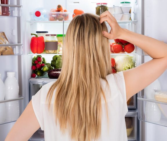 Kvinde kigger ind i sit køleskab og finder madvarer hun ikke behøver have der