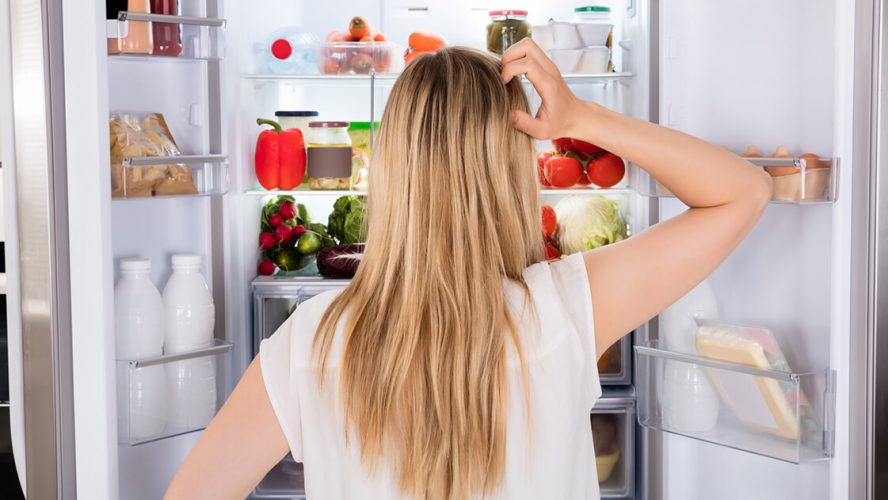 Kvinde kigger ind i sit køleskab og finder madvarer hun ikke behøver have der