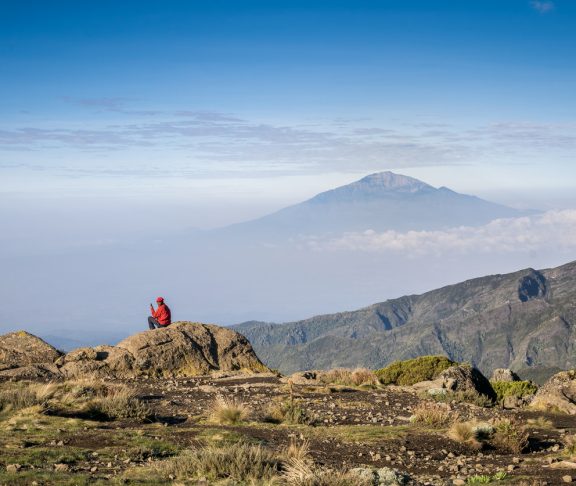 Man siting with his phone with view on Mount Meru, Tanzania