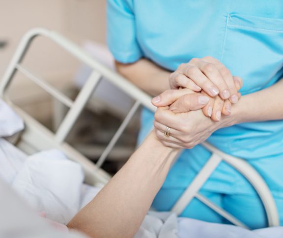 Midsection of female nurse holding senior woman's hand. Caring medical professional is with patient. She is consoling elderly woman in hospital.