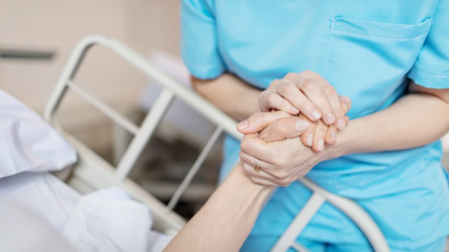 Midsection of female nurse holding senior woman's hand. Caring medical professional is with patient. She is consoling elderly woman in hospital.