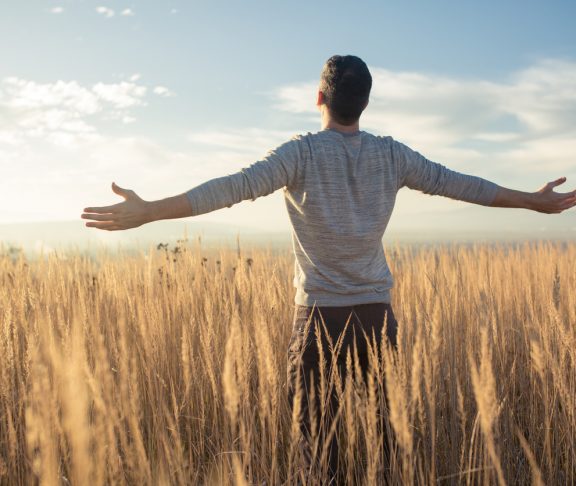 Young caucasian man standing in the middle of a prairie with his arms outstretched, enjoying a beautiful sunny day in the nature.