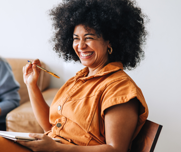 Black businesswoman smiling cheerfully while sitting in a meeting with her colleague. Happy young businesswomen working together in a modern workplace.