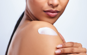 woman applying moisturiser to her shoulder against a grey background