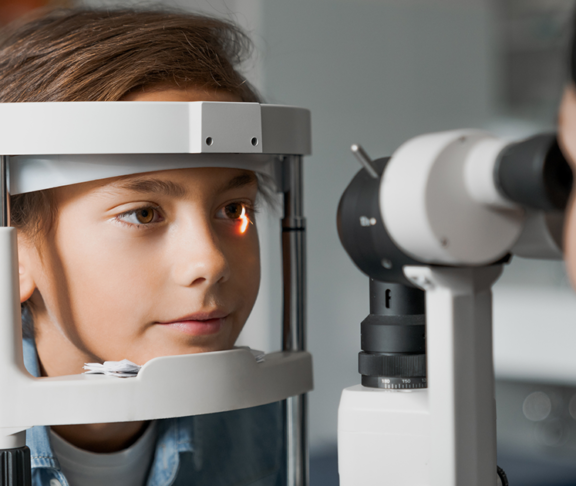 Adult female doctor ophthalmologist is checking the eye vision of cute child in modern clinic