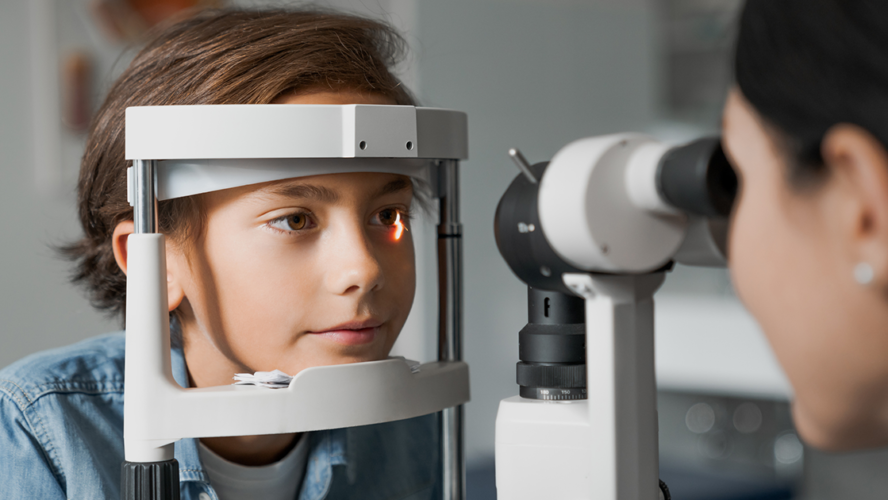 Adult female doctor ophthalmologist is checking the eye vision of cute child in modern clinic