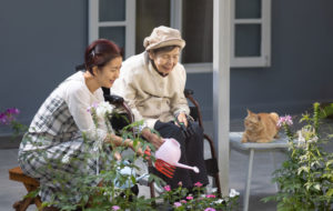 Elderly woman gardening in frontyard with daughter and cat