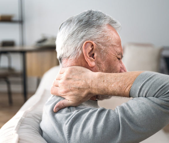 Elderly man rubbing hard pain in neck and massaging tense muscles
