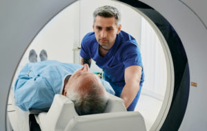 Senior man going into CT scanner. CT scan technologist overlooking patient in Computed Tomography scanner during preparation for procedure