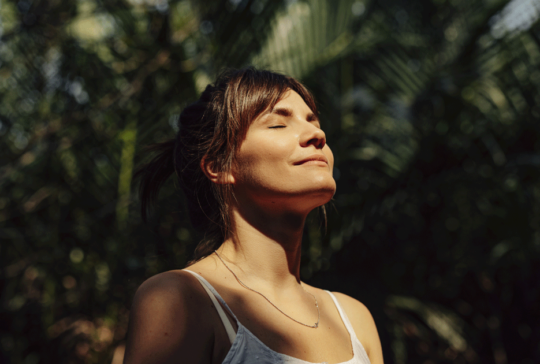 Beautiful Happy Woman Enjoying the Warm Sunlight in a Tropical Public Park