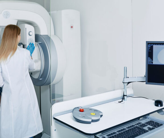 Mammogram procedure in medical clinic, mammography. Female mammologist positions mature woman at imaging machine to receive mammogram