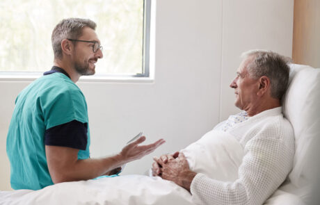 Surgeon Visiting And Talking With Senior Male Patient In Hospital Bed In Geriatric Unit