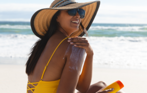 Smiling mixed race woman on beach holiday using sunscreen cream