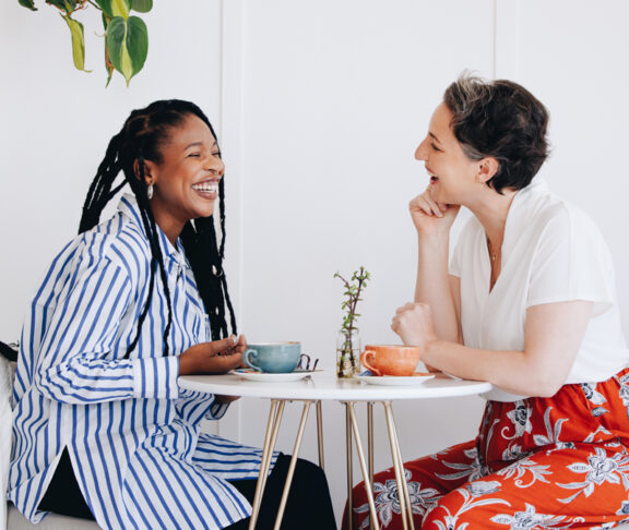 Two happy businesswomen chatting and laughing together during a coffee break in a cafe. Cheerful female business colleagues enjoying a friendly conversation in a coffee shop.