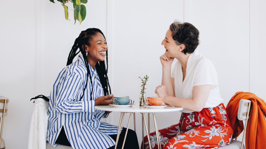 Two happy businesswomen chatting and laughing together during a coffee break in a cafe. Cheerful female business colleagues enjoying a friendly conversation in a coffee shop.
