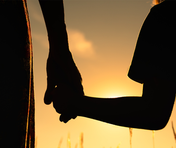 silhouette of mother and child holding hands facing the sunset