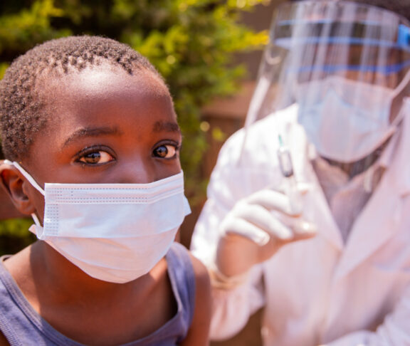 Portrait of a child in a clinic in Africa about to be vaccinated with the doctor beside him. - stock photo