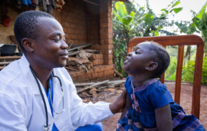 African doctor talking to a sick baby girl during a visit in a rural area in Africa - stock photo