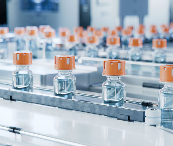 Glass Vials with Orange Caps on Conveyor Belt at Vaccine Production Facility. Medication Manufacturing Process. Medical Ampoule Production Line at Modern Pharmaceutical Factory
