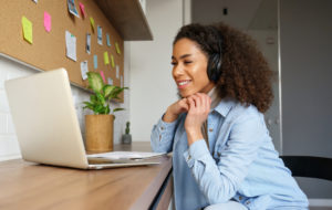 Smiling young african american teen girl wear headphones video calling on laptop. Happy mixed race pretty woman student looking at computer screen watching webinar or doing video chat by webcam.