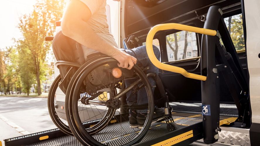 A man in a wheelchair on a lift of a vehicle for people with disabilities.