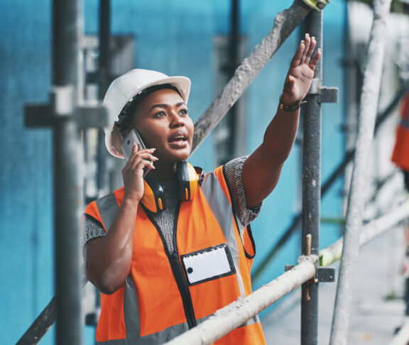 Shot of a young woman talking on a cellphone while working at a construction site.