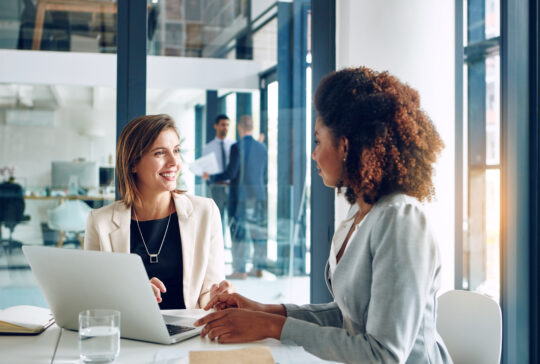 Business people, laptop and women in office for training planning and project idea, research or collaboration. Coaching, support and girl with manager for learning, discussion and problem solving