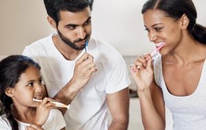 Family of three happily brushing their teeth together