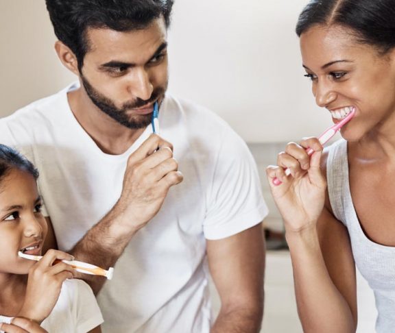 Family of three happily brushing their teeth together