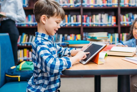 Dreng leger med iPad på skolebiblioteket