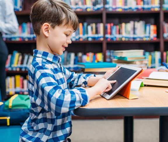 Dreng leger med iPad på skolebiblioteket