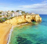 Sandy beach between cliffs in front of charming white architecture of Carvoeiro and turquoise Atlantic Ocean, Algarve, Portugal