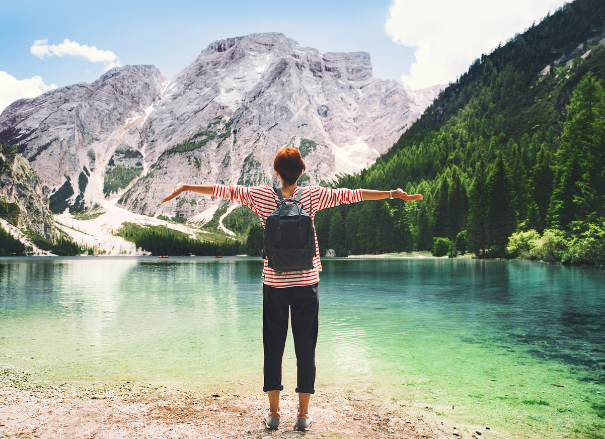 Woman with raised arms up looking at Braies Lake with mountains on background. Girl enjoying stunning view of Lago di Braies in Dolomites, South Tyrol, Italy, Europe. Beauty of nature image.