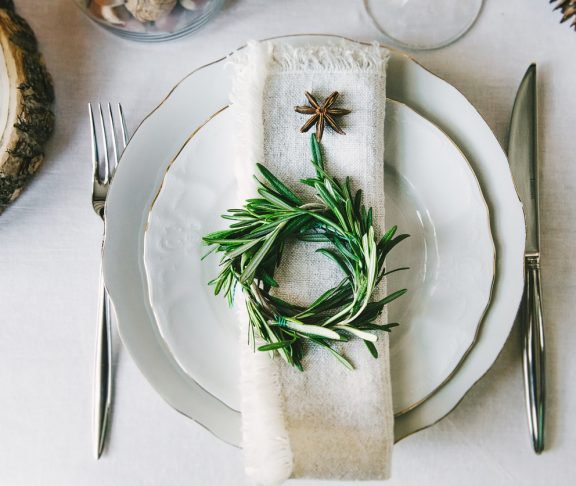 Decorative green wreath on a napkin as a part of table appointments, clean white tablecloth background, top view. Christmas table place setting.