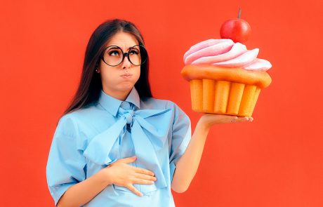 Kvinde holder sig på maven med oversize glutenfyldt cupcake i hånden