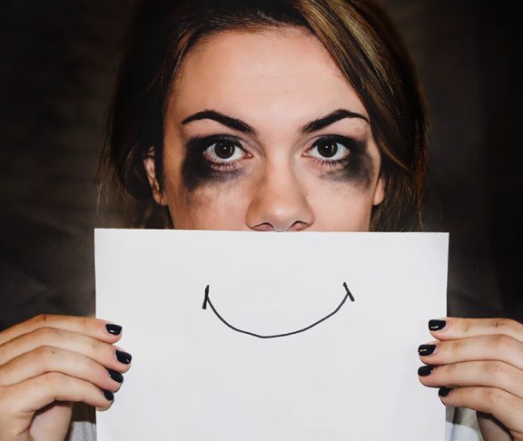 Kvinde med mascara under øjnene holder tegnet smil op foran munden