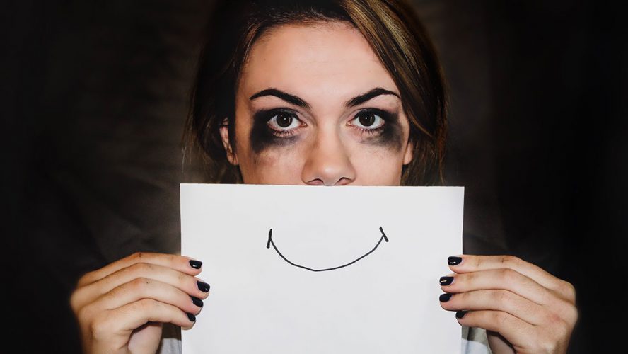 Kvinde med mascara under øjnene holder tegnet smil op foran munden