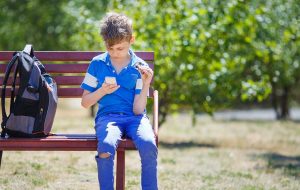 Dreng sidder på en bænk med sin rygsæk og kigger på sin telefon